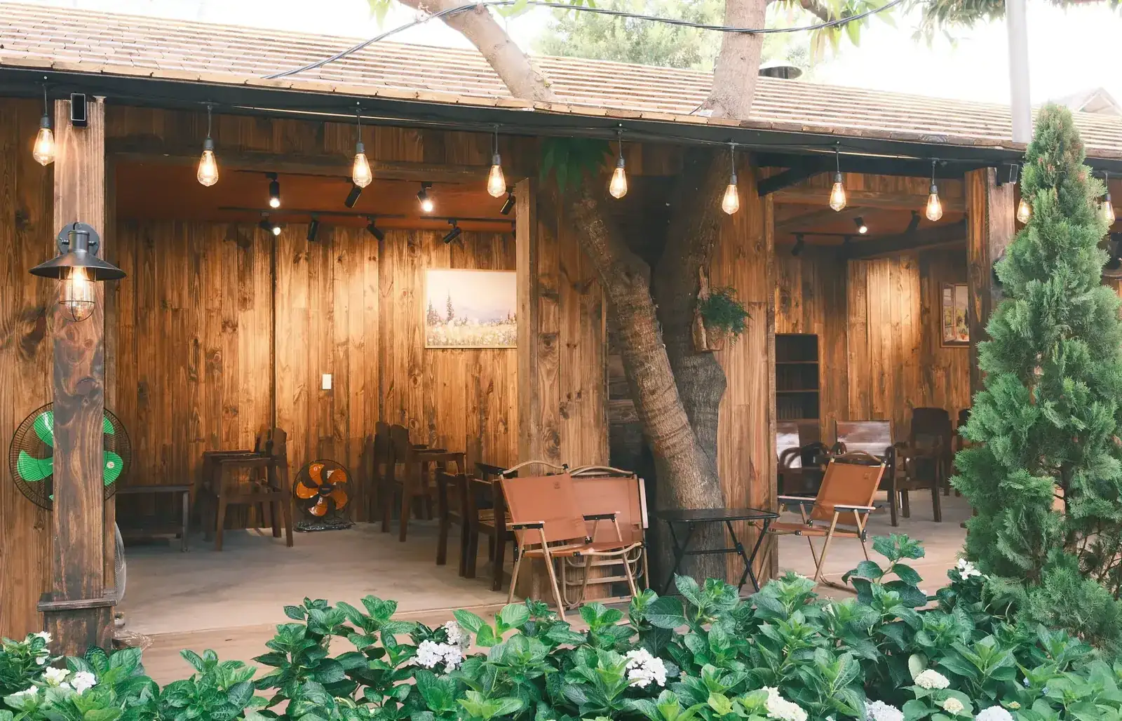Rustic covered wood patio surrounded by greenery and warm string lighting