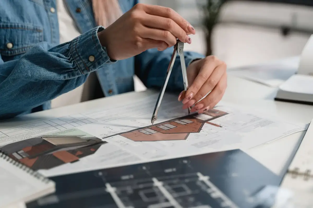 A creative professional using a compass on blueprints at an office desk