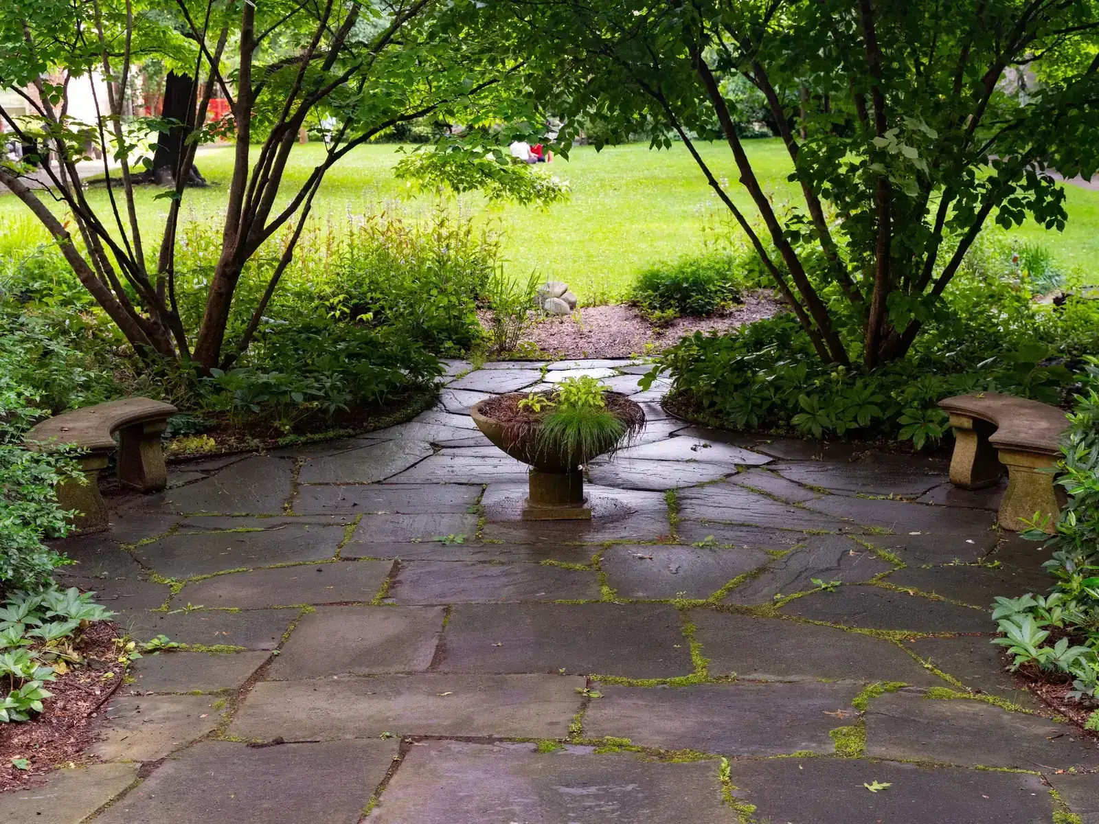 Wooded stone patio surrounded by mature greenery and a central planter