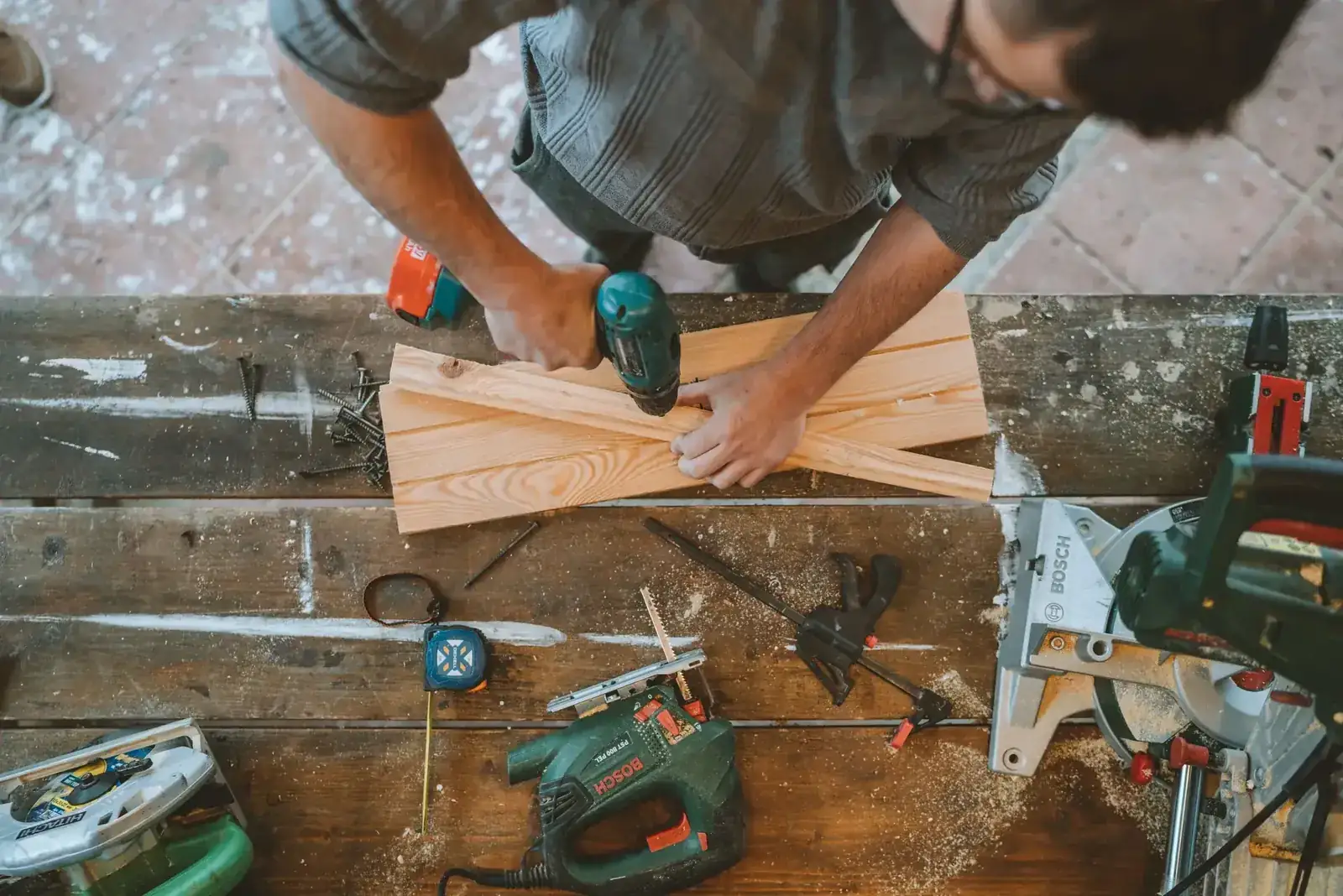 Craftsman busy drilling wooden planks in a carpentry workshop with various tools around