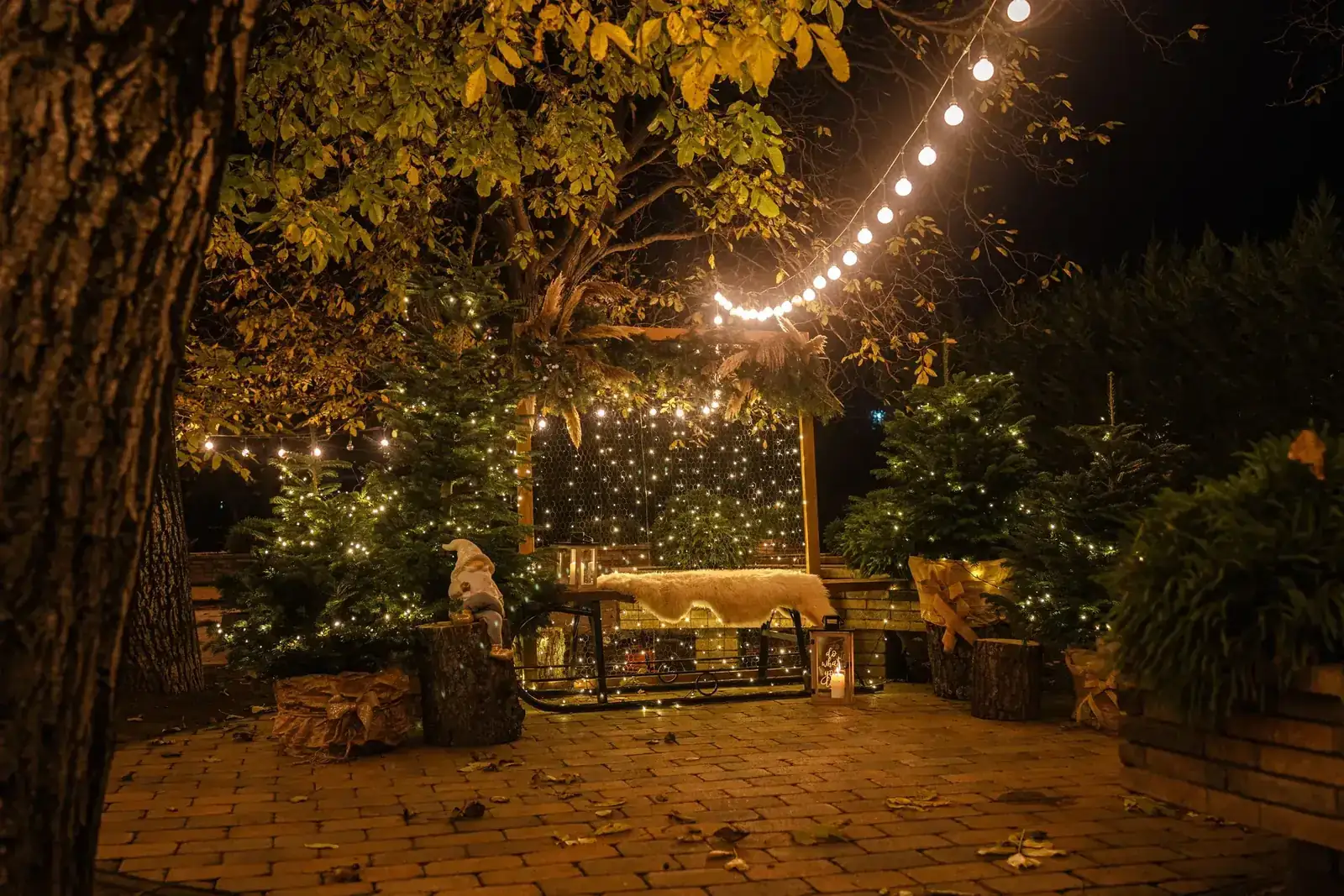 A cozy outdoor patio adorned with Christmas lights and decorations, creating a warm festive ambiance at night