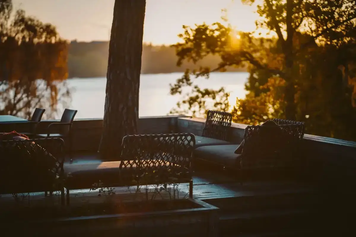 Woven patio seating overlooking a calm wooded lake at sunset