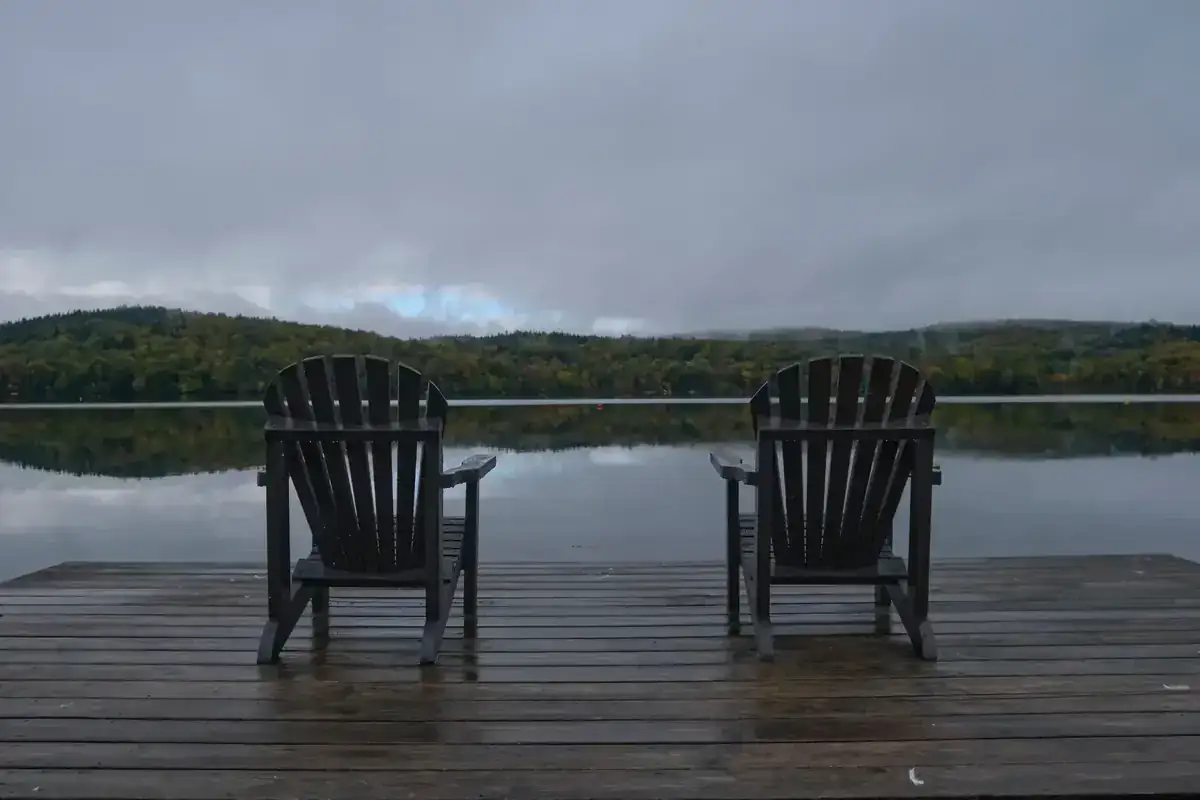 Two Adirondack chairs on a wooded dock overlooking a quiet lake
