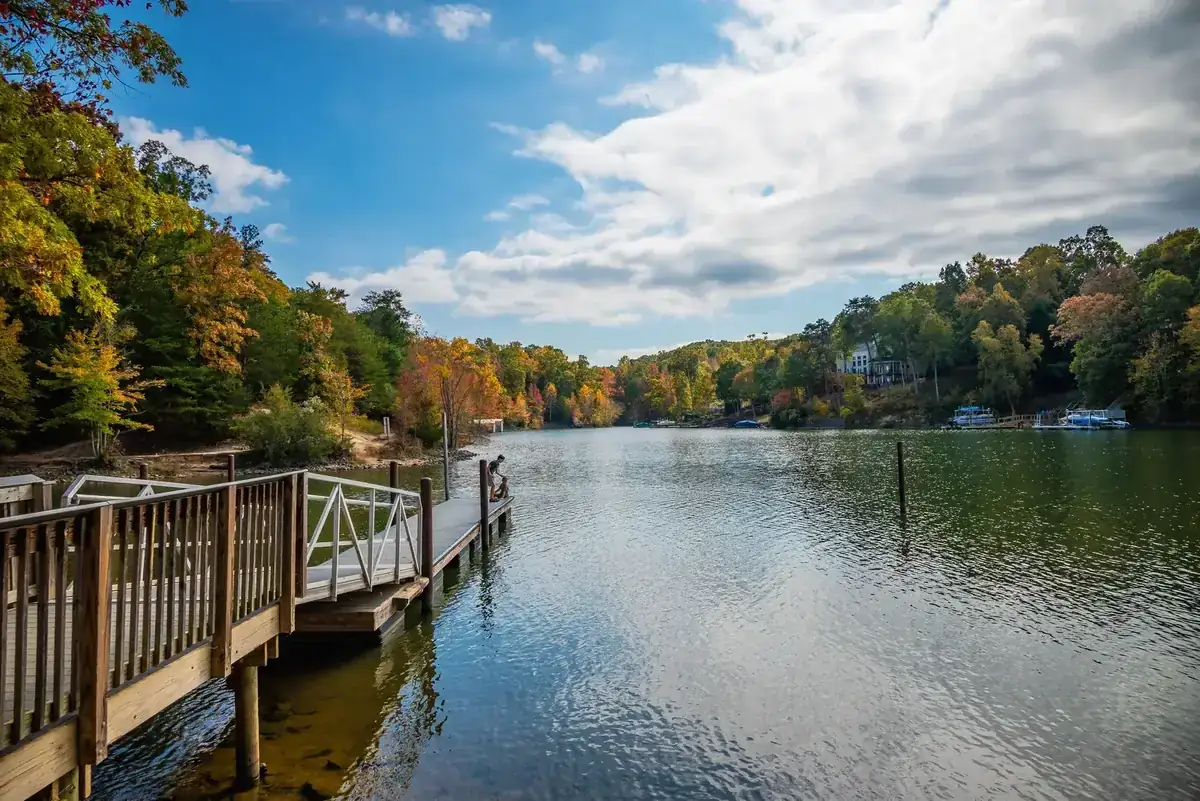 Peaceful lake with dock, surrounded by autumn trees and distant houses