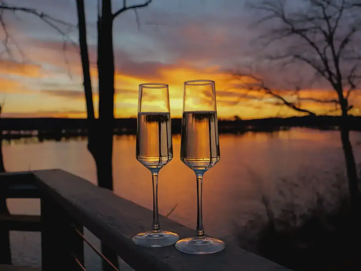 Two glasses on a deck railing at sunset overlooking a wooded lake