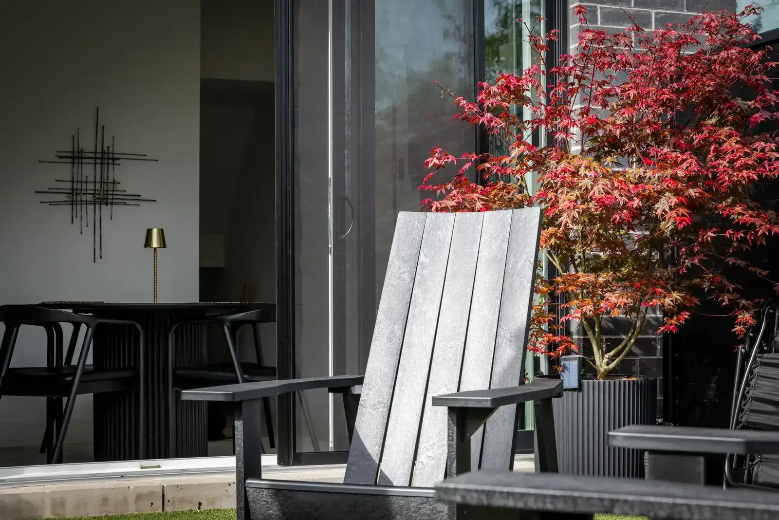 A serene outdoor patio featuring a sleek Adirondack chair beside a vibrant Japanese Maple tree
