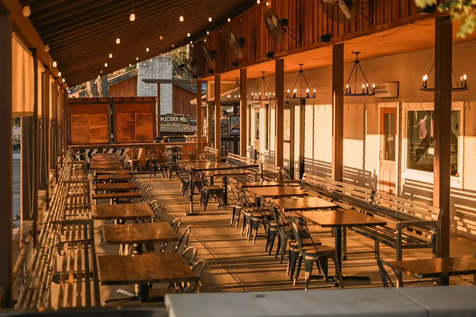 Warm and inviting outdoor patio area with wooden tables, chairs, and ambient lighting, perfect for dining
