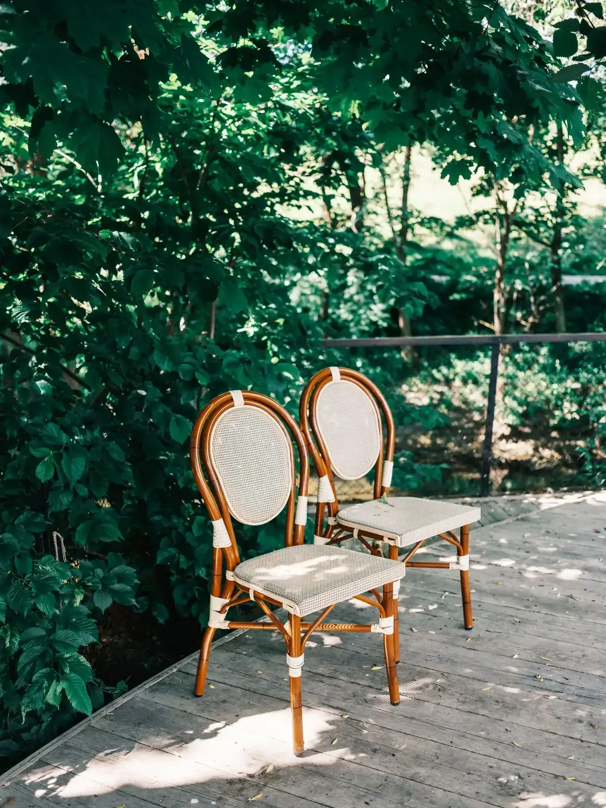 Two elegant wooden chairs on a sunny wooden deck amidst lush greenery
