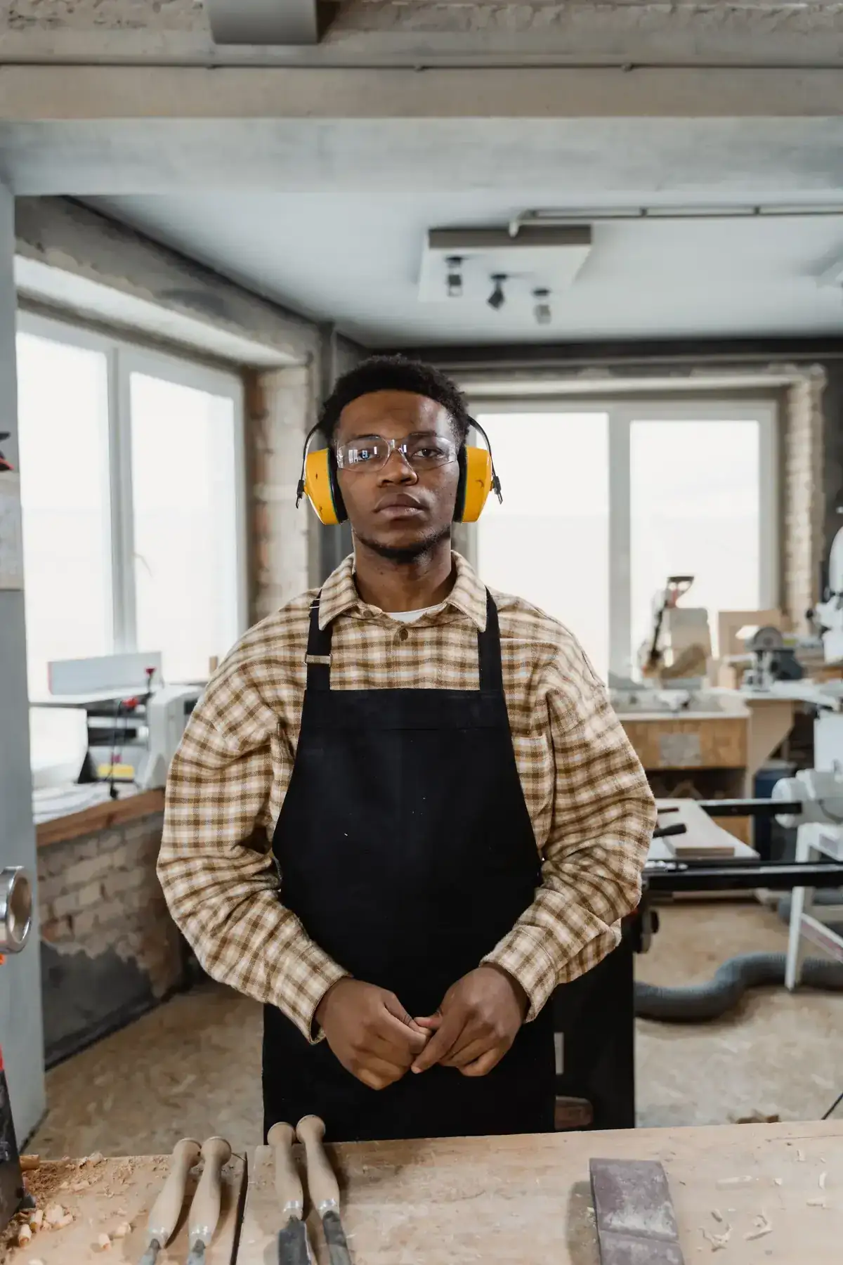 Professional woodworker wearing safety gear in a workshop, surrounded by tools and equipment