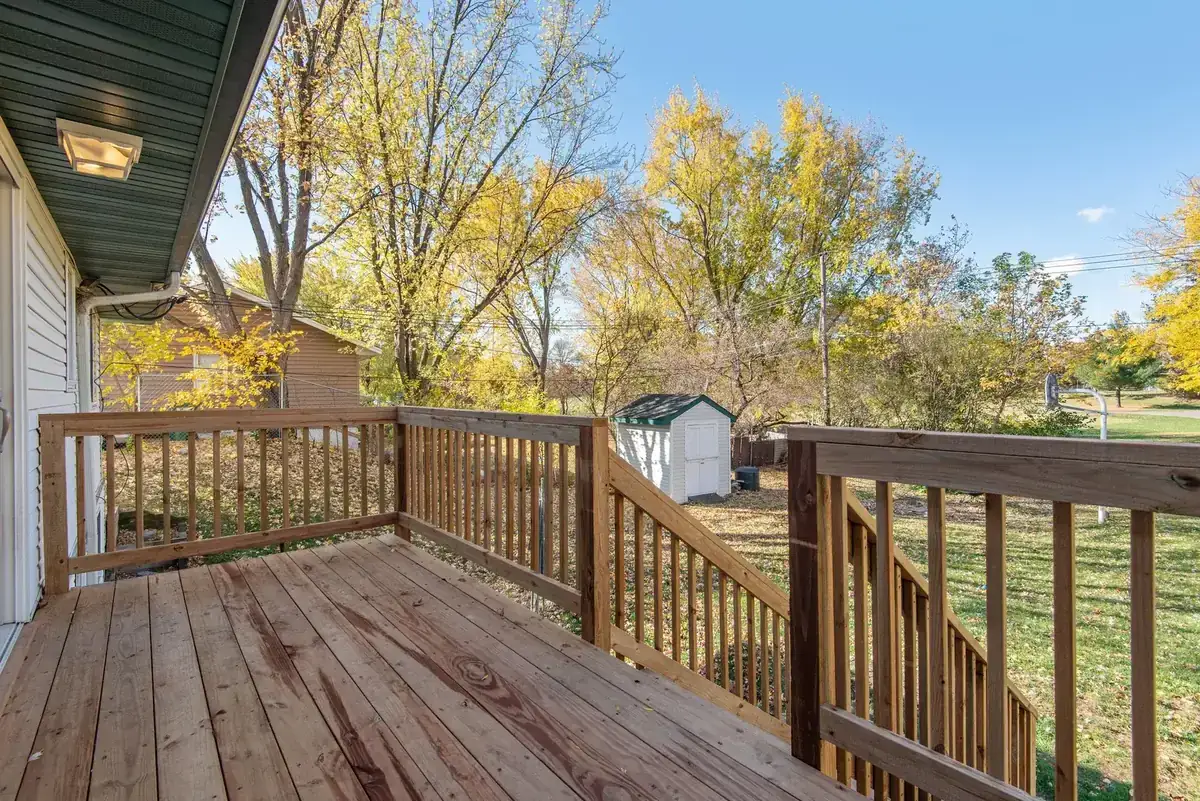 A spacious wooden deck with a view of a vibrant autumn backyard, perfect for relaxation