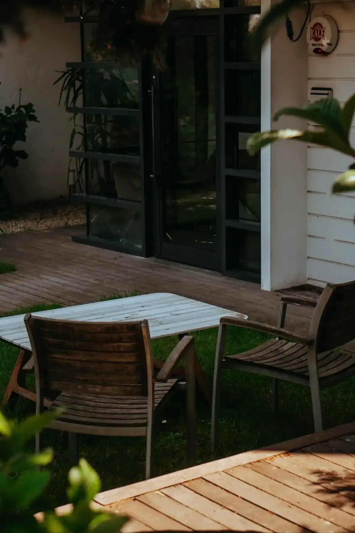 A tranquil outdoor patio featuring wooden chairs and table with greenery surrounding
