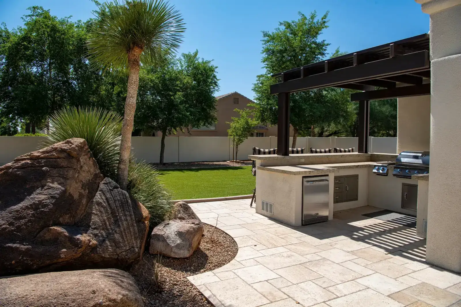 Stylish outdoor kitchen on a sunny patio with lush landscaping and clear blue sky