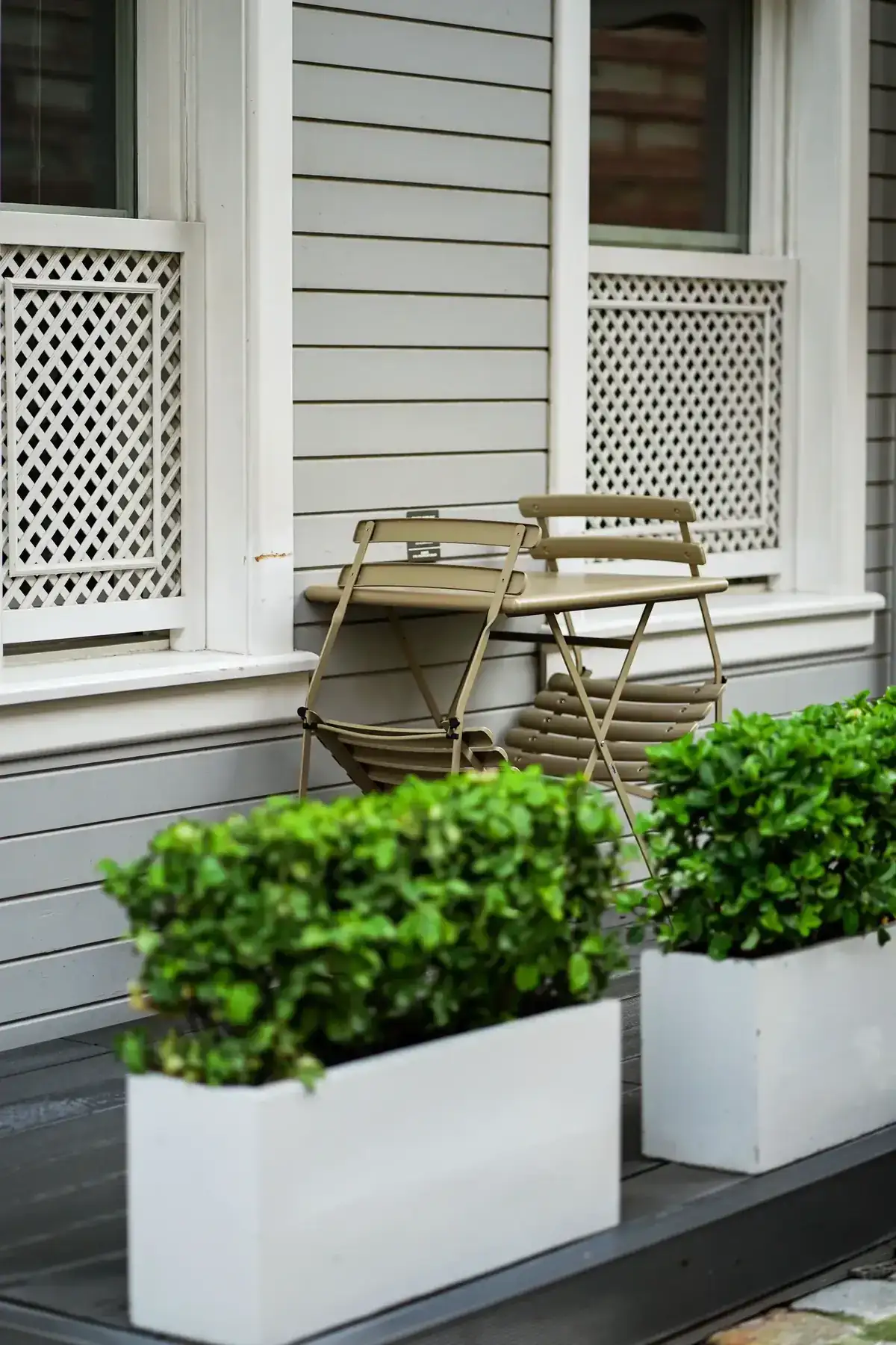 A contemporary patio featuring stacked foldable chairs and lush greenery in planters against a stylish house exterior