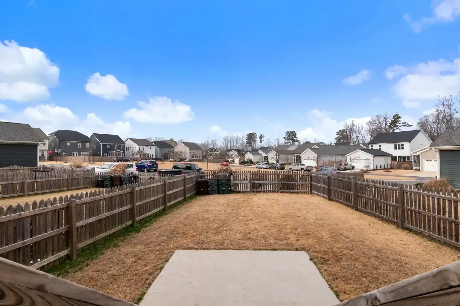 A suburban backyard with wooden fencing and modern houses under a blue sky